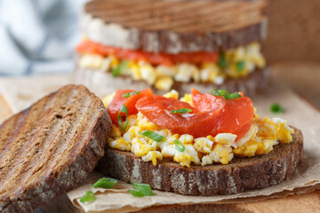 Scrambled eggs and smoked salmon on rye bread with green onions. A sandwich for breakfast. Selective focus - 570847890