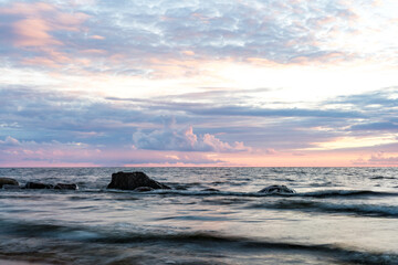 Long exposure of the baltic sea at dusk with rocks and breaking wavese in the foreground