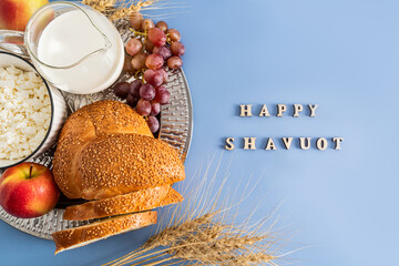 the spring holiday of the Jews of Shavuot. a festive card with traditional food and ears of corn. wooden letters on a blue background - happy shavuot.