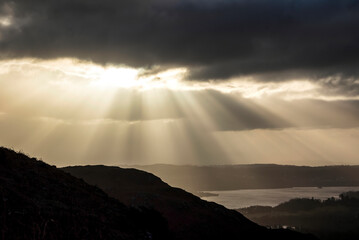 Fototapeta na wymiar Stunning Winter sunrise landscape view from Loughrigg Fell across towards Windermere with stunning sun beams coming from the dark clouds above