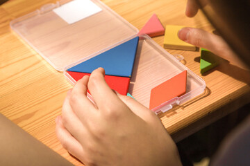 close-up of the hands of a child collecting a man from a puzzle in the form of multi-colored geometric shapes