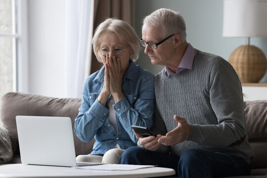 Shocked upset elderly couple getting bad news, finding fraud, money stealing, loss, overspending, financial problem, holding calculator, using laptop, staring at monitor