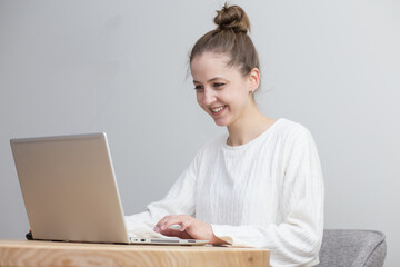 beautiful girl works at home at the table with a laptop in a white sweater on a white background