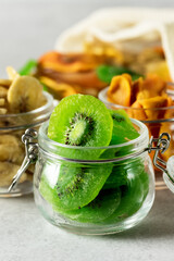 Green Kiwi Banana Persimmon Fruit Preserved in Glass Jars on Gray background Vertical