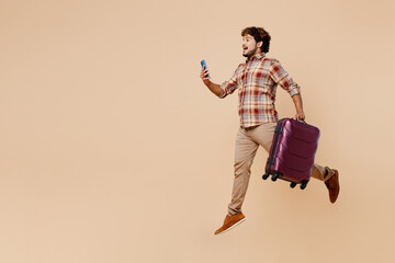 Shocked traveler Indian man wears casual clothes hold suitcase use mobile cell phone isolated on plain beige background Tourist travel abroad in free time rest getaway Air flight trip journey concept