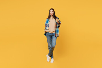 Full body fun young smiling woman wear blue shirt beige t-shirt hold takeaway delivery craft paper brown cup coffee to go isolated on plain yellow background studio portrait. People lifestyle concept.