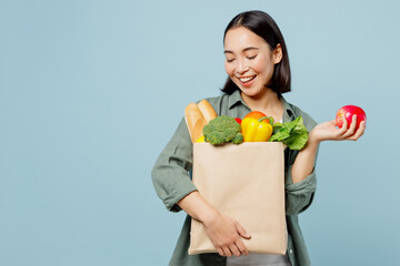 Young woman wear casual clothes hold apple look at brown paper bag with food products after...