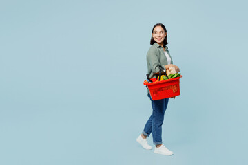 Full body side view young woman wear casual clothes hold red basket with food products look aside...