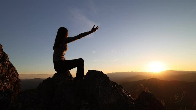 silhouette of a woman raising her hands while the sun is rising for worshiping God. Struggle. Victory. Praise to God spiritually and religiously. Success on the top of the mountain.4K slow motion.