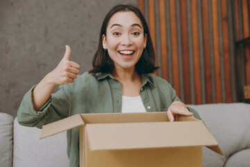 Young happy woman of Asian ethnicity wear casual clothes hold unpacking cardboard box show thumb up...