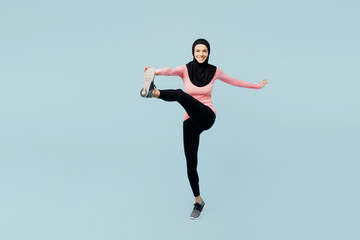 Fototapeta na wymiar Full body fun young asian muslim fitness trainer sporty woman wear pink abaya hijab spend time in home gym raise up leg stretch isolated on plain blue background studio Workout sport fit abs concept