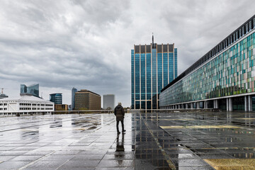 Lonely man in a city square on a rainy day. Cloudy urban landscape with reflections in the puddles...