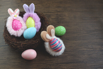 Top view of beautiful colorful Easter eggs wearing bunny rabbit ears headband in bird nest on rustic brown wooden surface background, decoration and celebration Easter and spring beginning.