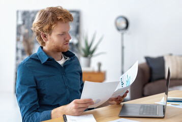 Young man entrepreneur, owner of a new business, working with reports, looks through documents,...