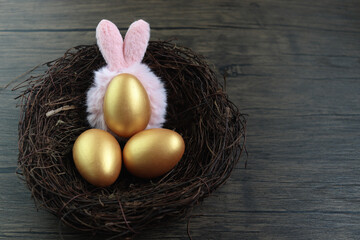 Top view of beautiful golden Easter eggs wearing bunny rabbit ears headband  in bird nest on rustic brown wooden surface background, decoration and celebration Easter and spring beginning.