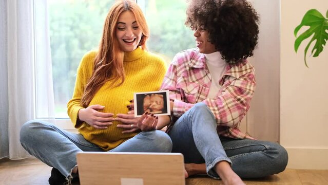 Two young women proud of their pregnancy teaching the ultrasound over the internet to their distant family. Concept: pride, motherhood, communication
