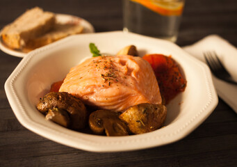steamed sea trout fillet served on fried mushrooms with tomatoes in a white bowl