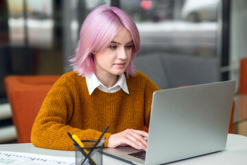 Young modern woman freelancer or entrepreneur working remotely using laptop while sitting in coworking space or home