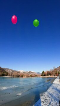 immersive view juggling with 4 balls (green, pink, yellow, orange) next to frozen lake. Snow on the ground. Mountains in background. Vertical footage, point of view from the chest, fish eye effect.