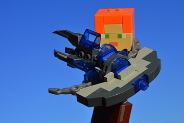 Fototapeta premium LEGO Minecraft figure of Alex holding KREO model of Star Trek Vulcan Jellyfish spaceship, from famous science fiction movie and TV series, known as ship of Mr. Spock. Blue skies in background.