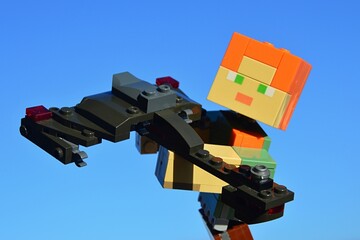 Fototapeta premium LEGO Minecraft large figure of main female character Alex holding KREO model of Klingon spaceship Bird Of Prey from Star Trek movie and TV franchise. Blue winter skies in background, sunny day sunshin