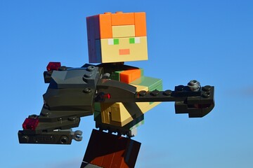 Fototapeta premium LEGO Minecraft large female figure of main character Alex holding model of Klingon battleship Bird Of Prey from Star Trek movie and TV franchise, made by KREO. Winter blue skies in background.