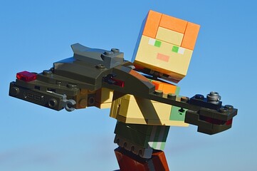 Fototapeta premium LEGO Minecraft large figure of female character Alex holding model of Klingon battleship Bird Of Prey from TV and movie series Star Trek, made by KREO. Blue winter skies in background.