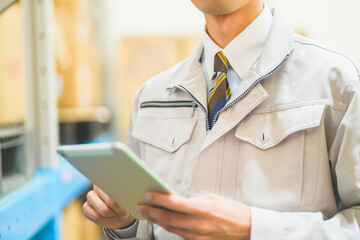作業服を着て倉庫で在庫管理をする若いビジネスマン