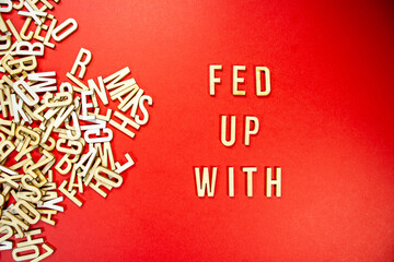 Fototapeta na wymiar FED UP WITH in wooden English language capital letters spilling from a pile of letters on a red background