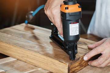 carpenter using nail gun or brad nailer tool on wood box in a workshop ,furniture restoration woodworking concept. selective focus - obrazy, fototapety, plakaty