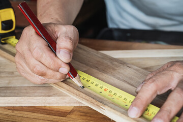 Carpenter using a measuring tape and mark a cut line with pencil on a wood board.DIY maker and...