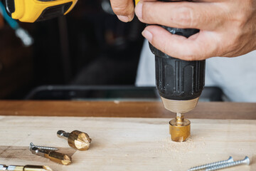 Carpenter use countersink bit to drill both a pilot hole and use countersink bit to recess the head of the screw into wood plank. DIY maker and woodworking concept. selective focus
