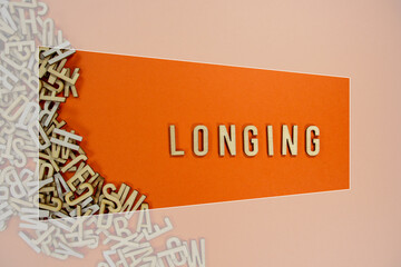 LONGING in wooden English language capital letters spilling from a pile of letters on a orange background framed