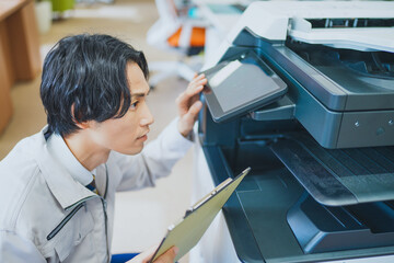 オフィスでコピー機の点検をする若いエンジニアの男性