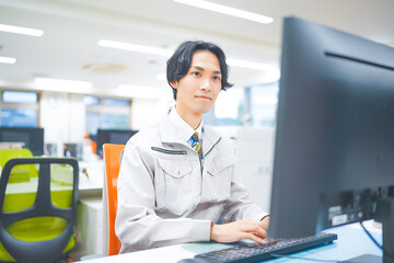 作業着を着てパソコン作業をする若いエンジニアの男性