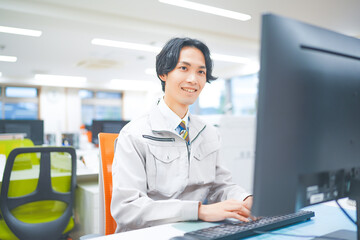 作業着を着てパソコン作業をする若いエンジニアの男性