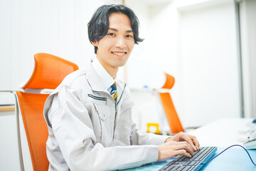 作業着を着てパソコン作業をする若いエンジニアの男性