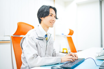 作業着を着てパソコン作業をする若いエンジニアの男性