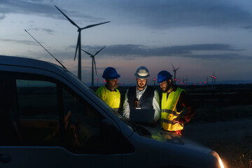 Team of technicians and engineer working in wind turbine farm at night, planing renewable energy...