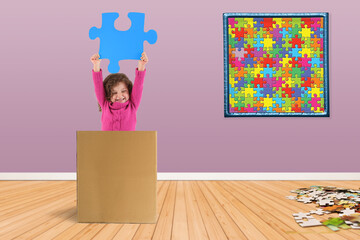 Kind iin einem Karton und hält ein Puzzleteil hoch