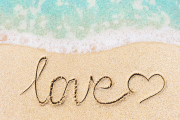 Love word written on sand surface with soft ocean wave on background