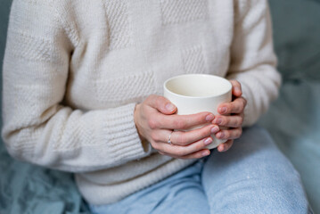 Young woman in white sweater and blue jeans sitting on the blue sofa and holding  in her hands...