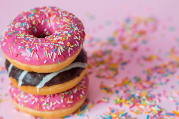 Delicious dessert. Pink, white and chocolate donuts with multicolored sprinkles on a pink background of Sweets. Confectionery products.