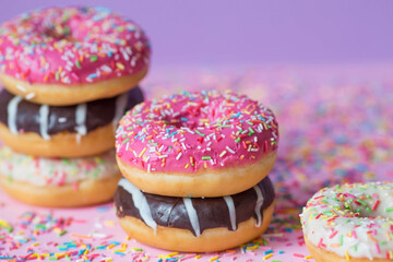 Delicious dessert. Pink, chocolate and white donuts with multicolored sprinkles on a purple...