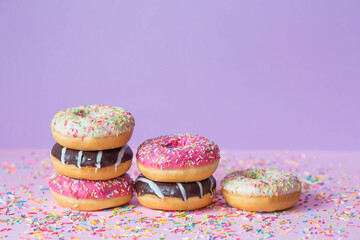 Delicious dessert. Pink, chocolate and white donuts with multicolored sprinkles on a purple background of Sweets. Confectionery products.