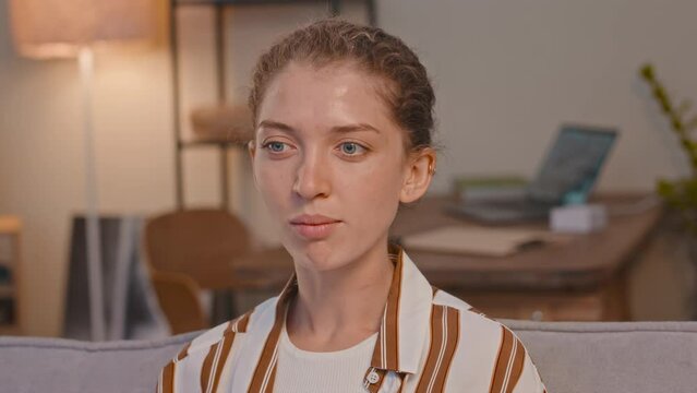 Chest up of young delighted Caucasian woman eating popcorn and laughing while watching funny TV program at home in evening