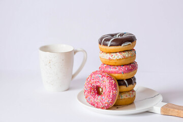 Delicious dessert. Pink, white and chocolate donuts with multicolored sprinkles, a cup of black coffee or tea. Sweets.