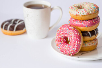 Delicious dessert. Pink, white and chocolate donuts with multicolored sprinkles, a cup of black coffee or tea. Sweets.