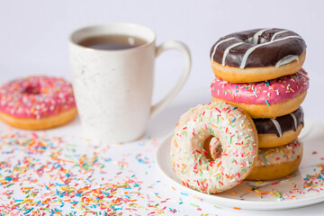 Delicious dessert. Pink, white and chocolate donuts with multicolored sprinkles, a cup of black coffee or tea. Sweets.