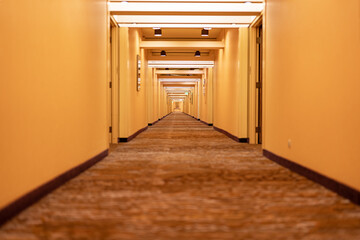 Long hotel corridor, hallway, with doors, carpet and yellowish beige tone.
